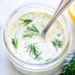 A jar of homemade dill ranch dressing with fresh dill and lemon.