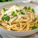 Lemon garlic pasta with shredded rotisserie chicken, topped with Parmesan and parsley in a white bowl.