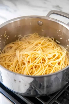 Cooked spaghetti in a stainless steel pot on a stove, ready to be mixed with sauce.