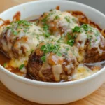 Cheese-covered meatballs in a savory onion sauce, served in a white bowl.