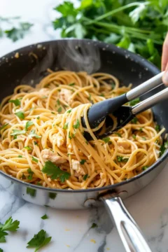 Leftover rotisserie chicken pasta no cream being tossed in a pan with tongs and fresh parsley.