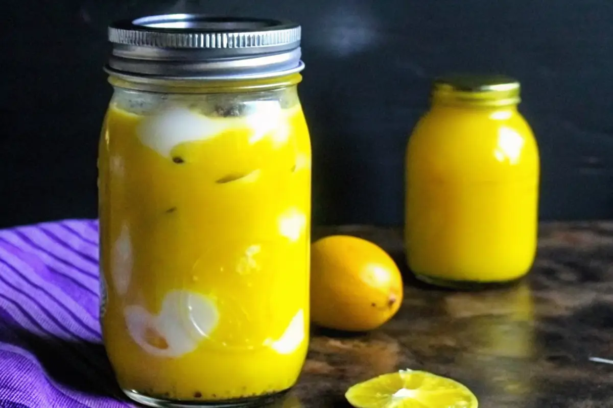 Jar of mustard pickled eggs with a vibrant yellow brine, placed on a dark surface with lemons in the background.