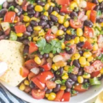 A close-up of Redneck Caviar served with a tortilla chip, featuring black beans, corn, tomatoes, and fresh cilantro.