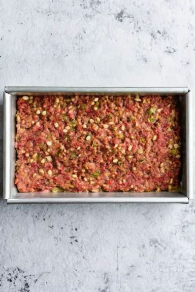 Close-up of two slices of juicy meatloaf with a glossy ketchup glaze, served over creamy mashed potatoes.