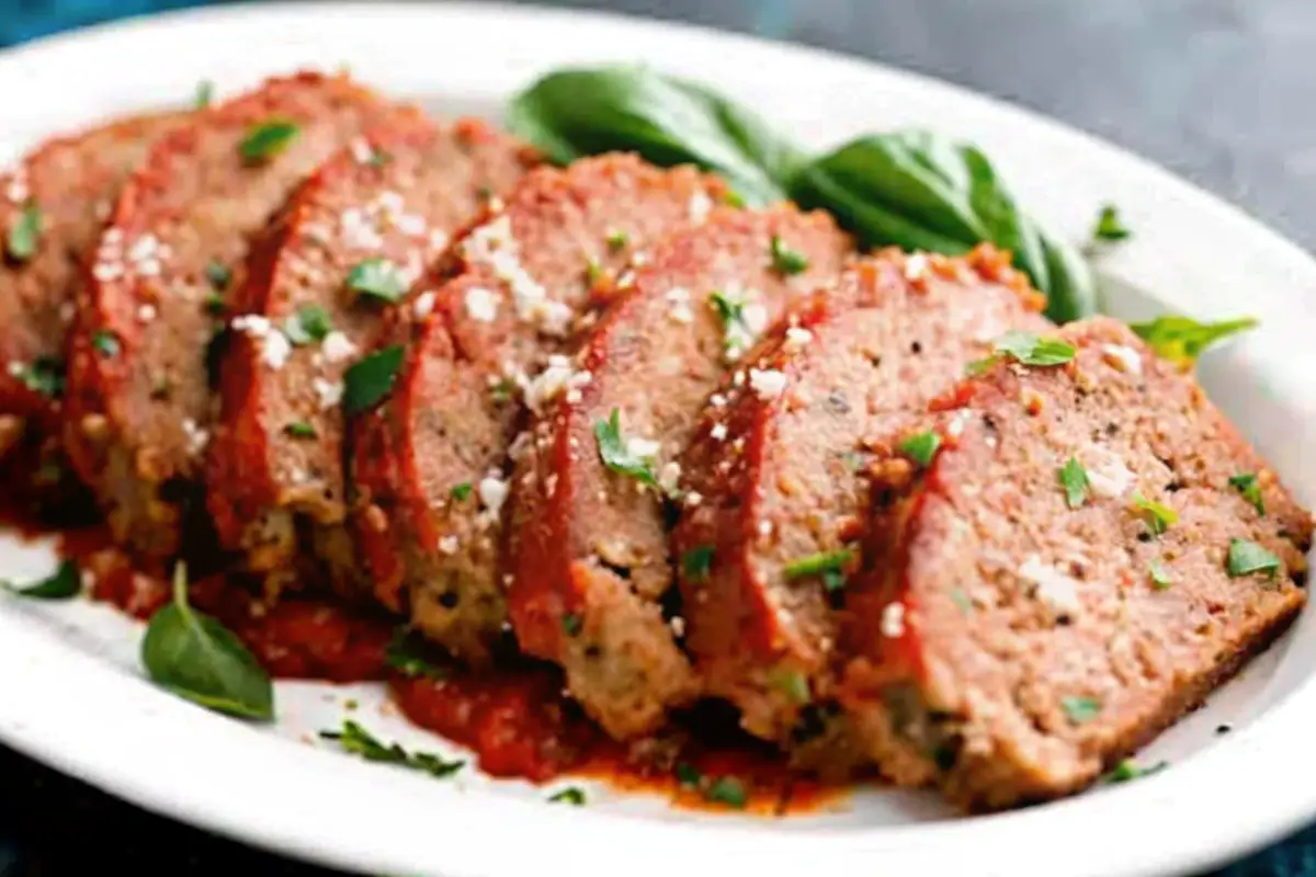 Sliced Italian meatloaf topped with marinara sauce, parmesan cheese, and fresh basil on a white plate.
